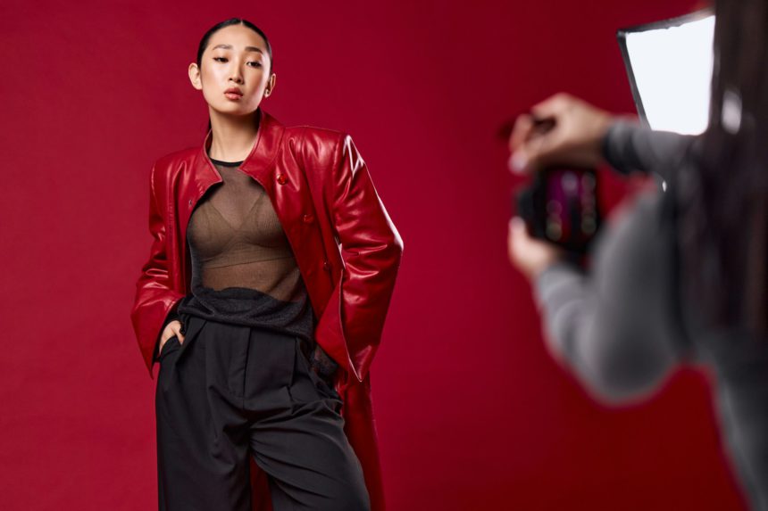 Fashion asian woman taking a photo of another woman in stylish outfit against red background